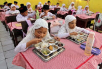 Siswa menyantap makan bergizi gratis di Sekolah Madrasah Ibtidaiyah Negeri Medan, Sumatera Utara, Rabu (14/1/2026).
