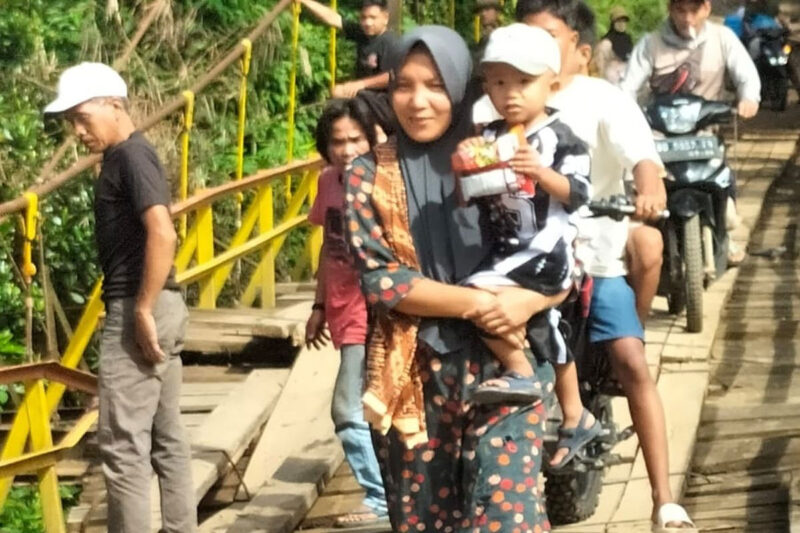 Seorang ibu menggendong anaknya saat melintas di jembatan gantung Desa Talang Buai, Kabupaten Mukomuko, Bengkulu.(Asril)
