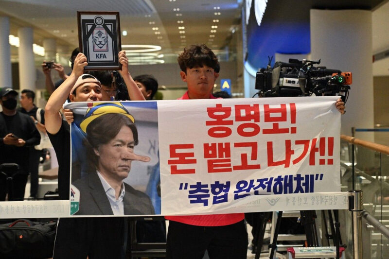 Seorang pria memegang spanduk bertuliskan Hong Myung-bo! Ludahkan uangnya dan keluar! Bubarkan KFA sambil menunggu kedatangan pelatih kepala timnas Korea Selatan, Hong Myung-bo, yang telah mengumumkan pengunduran dirinya setelah timnya tersingkir di babak penyisihan grup Piala Dunia FIFA 2026, di Bandara Internasional Seoul-Incheon, Incheon pada 30 Juni 2026. Kekalahan telak Korea Selatan di babak pertama Piala Dunia telah memicu kemarahan di dalam negeri dan seruan untuk perombakan total di pucuk pimpinan belum mereda setelah pengunduran diri pelatih. Pelatih Korea Selatan mengundurkan diri pada 28 Juni 2026, sehari setelah timnya tersingkir dari babak penyisihan grup Piala Dunia dan setelah mendapat kecaman dari presiden negara tersebut.(AFP/JADE GAO)
