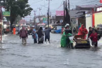 Warga mendorong sepeda motor yang mogok saat melintasi banjir di kawasan Lubuk Lintah,Kuranji Kota Padang, Senin (3/8/2026).(Rahmat Panji (Kompas.com))
