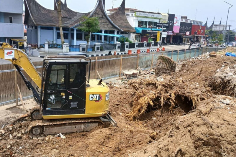 Alat berat bekerja meratakan lahan dan mengeluarkan tunggul pohon pinus setelah pohon berusia puluhan tahun ditebang untuk revitalisasi taman depan Kantor DPRD Kota Bukittinggi, Jumat (04/09/2026).(KOMPAS.COM/DHARMA HARISA)

